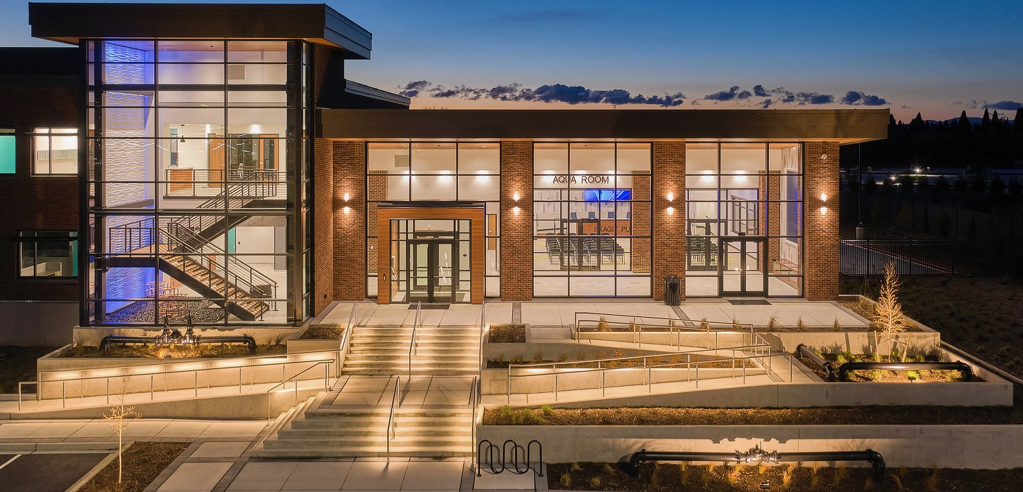 Glazed commercial building with a lit glass stair tower at dusk
